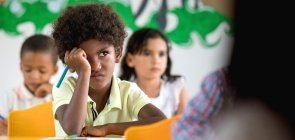 Estudante sentado em sala de aula com expressão de descontentamento e agitação segura um lápis azul e olha para frente