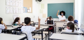 Uma turma de estudantes com os braços levantados em direção à professora