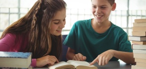 Uma aluna e um aluno sorriem enquanto leem um livro