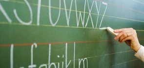 Mão de mulher escreve letras em uma lousa verde com giz branco