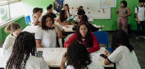 Alunos debatem durante aula e professora Lavini ao fundo acompanha as discussões
