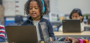 menino com fone de ouvido realiza tarefa em um notebook na sala de aula