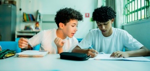 Estudantes dos Anos Finais sentados em dupla conversam sobre atividade que estão fazendo no livro