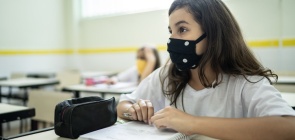 Uma aluna de máscara presta atenção à sua frente dentro de uma sala de aula