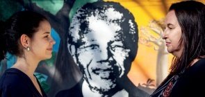 Duas educadoras de perfil se olham. No fundo um desenho do Nelson Mandela