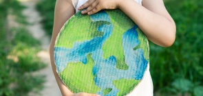 Foto de uma criança abrançando um desenho de um planeta terra. foto não mostra a cabeça da criança, só o recorte do abraço