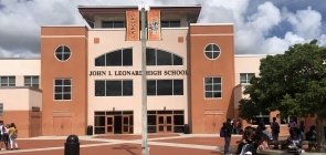 Uma construção grande retangular pintada de um rosa alaranjado. Na fachada do prédio está escrito 