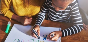 Menina escreve o alfabeto com canetinha e do lado a professora acompanha