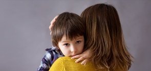 Menino triste carrega urso de pelúcia no colo da mãe