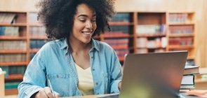 Mulher anota no caderno enquanto olha para o computador