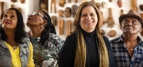 Foto da professora Nilma. Ela sorri. Ao lado dela, três alunos da EJA