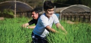 Foto de um aluno sorrindo e mexendo em uma plantação