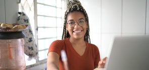 Uma adolescente estuda em frente ao computador, na cozinha de sua casa