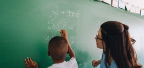aluno resolve operações matemáticas na lousa e professora orienta