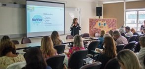 Cristiana Berthoud lança campanha da undime. Mulher em pé discursa na frente de sala. Ao seu lado, uma apresentação com o público alvo da campanha A escola na vibe da #paz 
