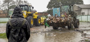 Foto de uma pessoa olhando para uma escavadeira retirando o lixo após as enchentes 