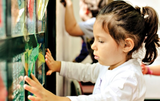 Menina observa vitrais feitos com papel celofone e vidro