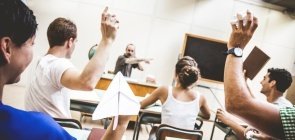 Alunos atiram papéis, cadernos e aviões de papel contra professor sentado em sua mesa na frente da sala