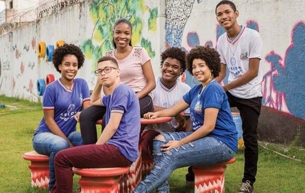 Ao ar livre, 6 jovens sentam em roda e sorriem