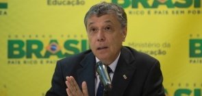 Um homem de cerca de 55 anos falando para um microfone sentado em uma bancada