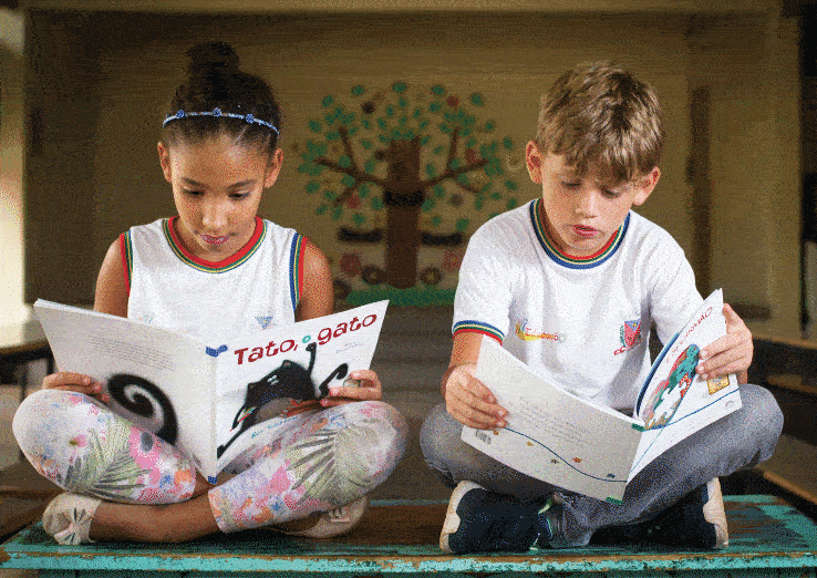 Anima&ccedil;&atilde;o alterando entre ilustra&ccedil;&atilde;o e fotografia de dois alunos lendo em espa&ccedil;o coletivo na escola.