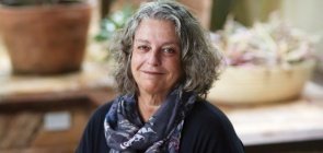 Mulher branca de cabelo grisalho na altura do ombro veste camiseta preta e um cachecol colorido