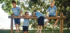 Quatro crianças escalam brinquedão. Elas usam uniforme, uma camiseta azul claro escrito Maristas e uma bermuda azul escuro