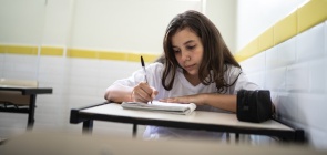 Menina de 12 anos está sentada em sala de aula, ela escreve