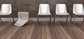 Cadeira branca caída em meio a fileira com outras cadeiras em sala com parede de concreto