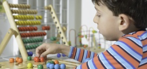 Aluno mexendo em objetos organizados em coleções, no fundo um ábaco colorido