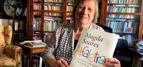 Professora Magda Soares segura a capa de seu novo livro