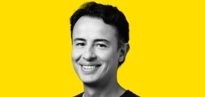 Fundo amarelo, foto em branco e preto. Homem entre 30 e 40 anos, de cabelo curto, sorrindo. 