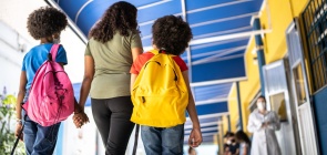 Mulher caminha de mãos dadas com duas meninas em direção à sala de aula