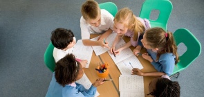 alunos sentados no formato de uma roda com uma mesa verde no centro, eles fazem atividade