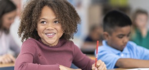 menina negra, sentada em uma carteira, sorri