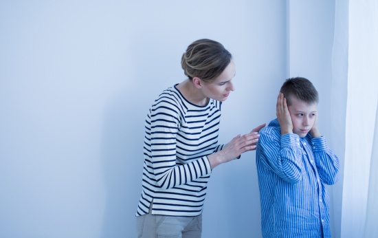 Menino com asperger tampa os ouvidos enquanto a mãe fala com ele.