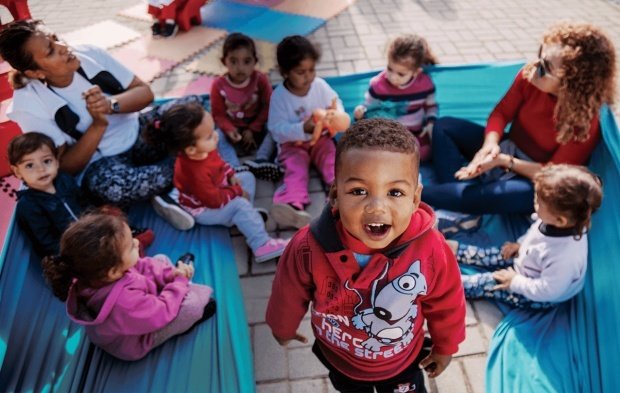 Foto de uma roda de conversa no chão. Uma criança está em pé e olha para a foto