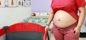 Menina grávida, ao lado de um berço