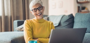 Educadora sorri. Ela está na frente do computador, é branca, com o cabelo grisalho curto