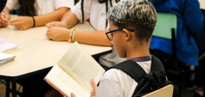 Sentado, aluno segura um livro aberto nas mãos