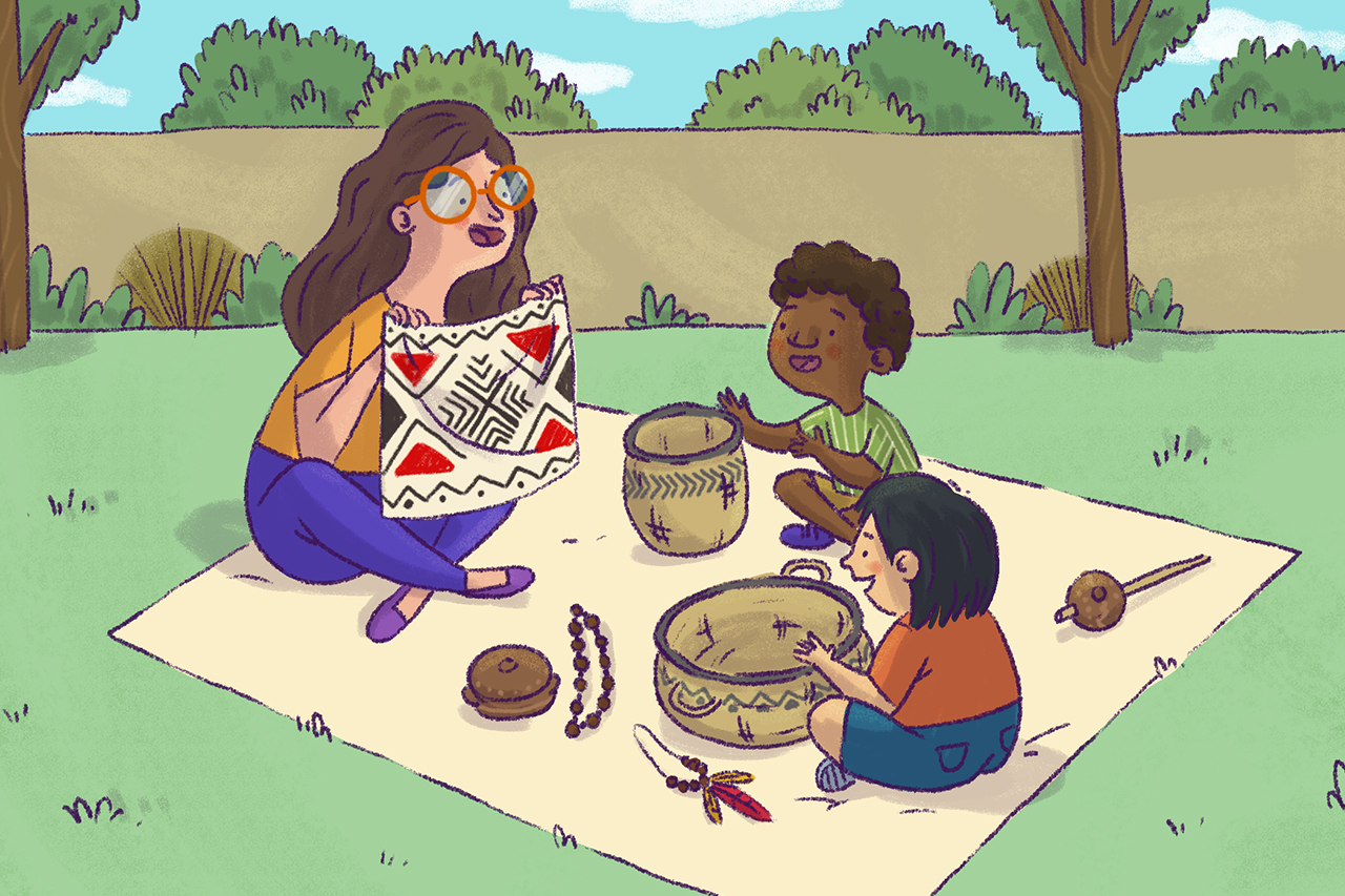 Professora de educa&ccedil;&atilde;o infantil, sentada sobre toalha no jardim junto aos alunos, mostrando alguns objetos de culturas ind&iacute;genas.
