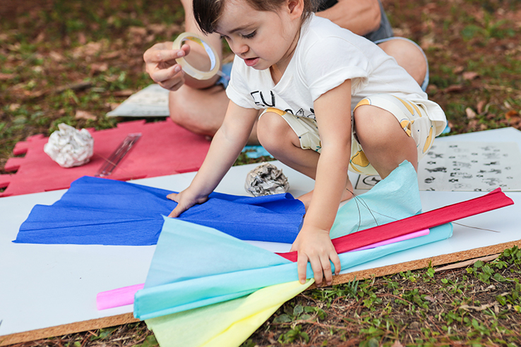 Fotografia de crian&ccedil;a brincando com objetos de largo alcance que est&atilde;o distribu&iacute;dos sobre a grama em um parque.