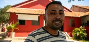 Foto de Antônio Araujo reconhecido como professor-inspiração de Quixeramobim. No fundo uma casa vermelha.