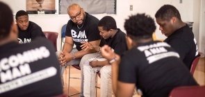 Homens negros em roda todos usam uma camiseta preta escrito BAM