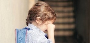 Menina chora no corredor da escola, com a mochila nas costas