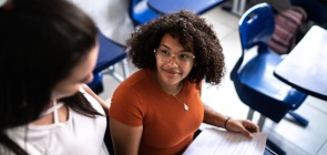 Jovem sentada em carteira olha para professora