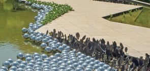 Esferas de vidro flutuam na água. Ao redor um caminho asfaltado e plantas