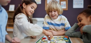 Grupo de crianças, entre 6 e 7 anos, jogam jogo de tabuleiro