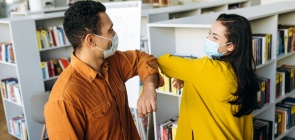 Um homem e uma mulher de máscara se cumprimentam com uma saudação nos cotovelos