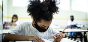 Aluna negra escreve. Ela usa máscara de proteção